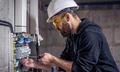 An electrician with a brown beard works on the electrical system in a commercial building