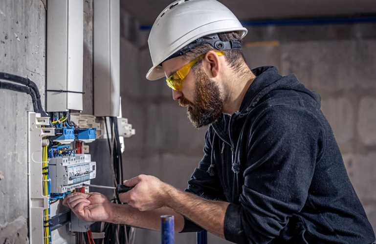 An electrician with a brown beard works on the electrical system in a commercial building